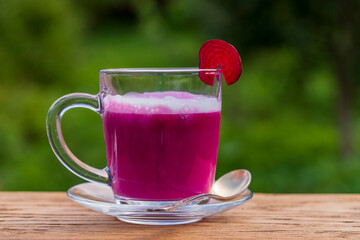 Pink beet latte from fresh beetroot juice blended with vanilla and milk in a transparent cup on the table in cafe on nature background, closeup, copy space. Trendy healthy vegetable drink