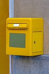 Yellow post office box hanging on building wall facade outside