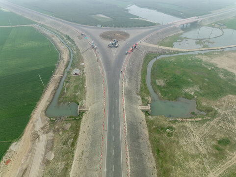 Aerial view of a Y intersection of newly built roads cutting through the landscape, creating a stark contrast with the surrounding greenery, Mithamain, Dhaka Division, Bangladesh.
