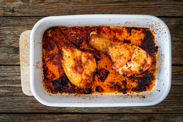Baked chicken drumsticks in baking dish on wooden table. Top view