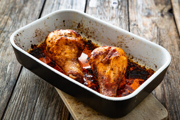 Baked chicken drumsticks in baking dish on wooden table