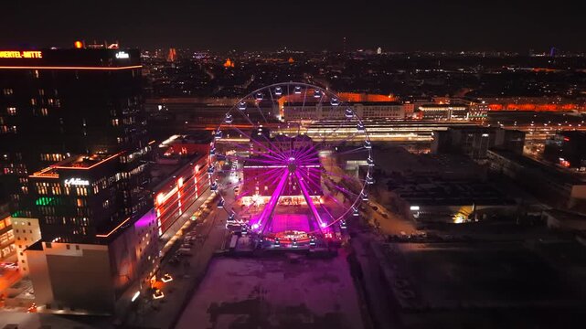 Aerial view of Munich at night showing Werksviertel modern quarter. Drone footage highlights illuminated Ferris wheel and vibrant city life. Umadum Riesenrad und urbanes Stadtbild nahe Ostbahnhof.