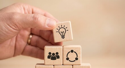 Close up of an adult hand building a wooden block pyramid with teamwork and innovation icons, representing professional leadership and community strategy in a bright minimalist indoor office setting.