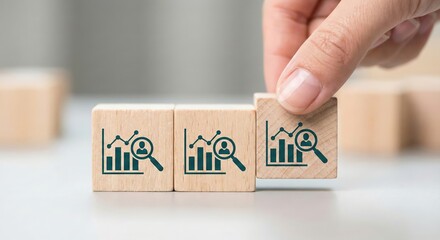 Professional adult placing wooden blocks with teal HR analytics icons, including bar charts and magnifying glass, for recruitment and talent acquisition strategy in a bright indoor office.