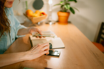Woman calculating household budget and managing finances, holding money and using a calculator to plan expenses, savings, and making payments for economic stability