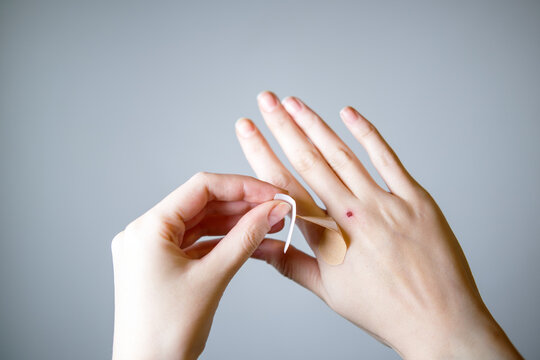 Female putting sticking plaster onto hand on gray background.