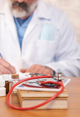 Doctor writing prescription with stethoscope and medicine on desk