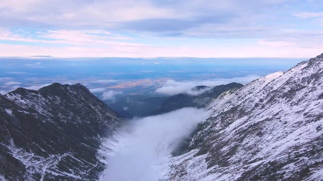 Aerial view of Transfagarasan road in Romania, in winter season. Video was shot from a drone while flying backwards at high altitude and lowering the camera to reveal the road and the valey.