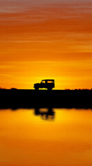 Silhouette of an off-road vehicle on the horizon at vibrant orange sunset with water reflection. Adventure travel, road trip freedom, minimal landscape, calm mood, and copy space background.