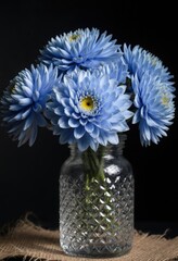 Vibrant blue dahlias in crystal vase on burlap against a black background