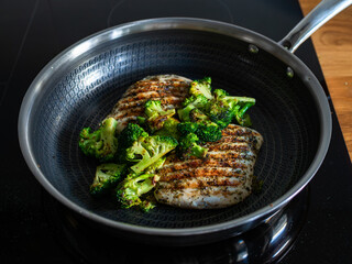 Grilled pork loin steaks and broccoli in frying pan on electric stove