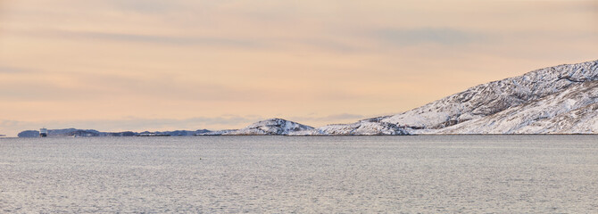 Landscape, travel and shoreline with mountains in background, rocky cliff and water in northern area. Nature, cold and tourism with sky backdrop, arctic and white outdoors in snowy wilderness banner