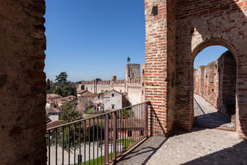 View through a medieval archway in Cittadella, Italy, revealing the central tower and historic rooftops under a clear sky.