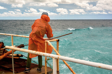 Girl in bright orange raincoat stands on stormy dock, contrasting vibrant humanity with raging sea.