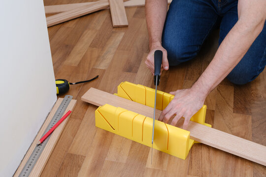 Handyman sawing wooden plinth using miter box