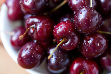 A mound of ripe cherries with stems lies in a fruit bowl. The fruits are red to dark red, covered...