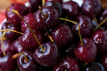 A mound of ripe cherries with stems lies in a fruit bowl. The fruits are red to dark red, covered in water droplets. Close-up of juicy cherries.