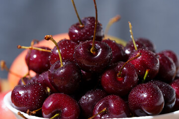 A mound of ripe cherries with stems lies in a fruit bowl. The fruits are red to dark red, covered...