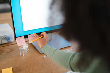 A person writes a note on a sticky note attached to a computer monitor, organizing their tasks for the day.