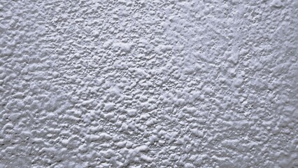 closeup rough plaster wall texture reveals granular stucco surface, subtle light and shadow, soft gray tones, uneven bumps