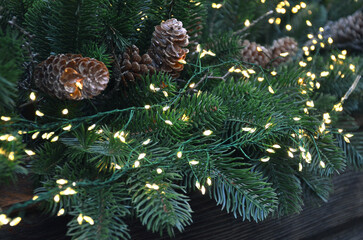 Winter holiday festive garland of artificial pine tree branch , brown cones and small yellow lights .Winter holiday ,Christmas, New Year celebration, concept.