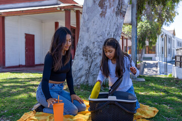 Mother and daughter opening their picnic basket on a blanket in the park