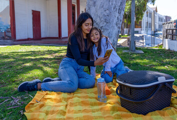 Mother and daughter laughing while connecting on a smartphone in a park