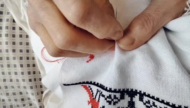 Process of hands stitching red cross-stitch embroidery on white linen fabric. Close-up video