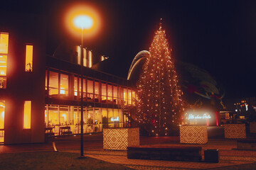 Christmas tree with festive lights in city square at night near modern building