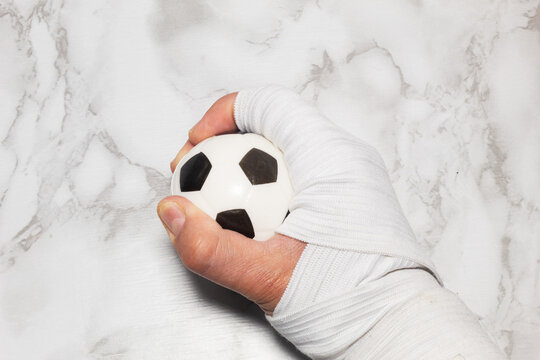 Bandaged hand holding a soccer ball on white marble surface, concept of sports recovery and self-care at home - Powered by Adobe