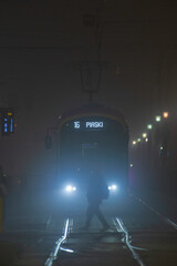 Mglista noc w Warszawie – tramwaj i sylwetka przechodnia w świetle reflektorów
