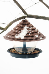 A plastic bird feeder with seeds and bird food hangs from a tree. Caring for birds in winter