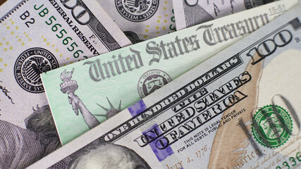 Close view of United States currency with United States Treasure check tax refund. The focus is on the hundred dollar note along with others in a mix of colors and designs. The detail highlights diffe