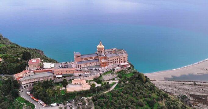 Aerial view of the Sanctuary of Tindari perched atop a cliff, showcasing the contrast between the golden dome and the turquoise waters, Tindari, Sicily, Italy.