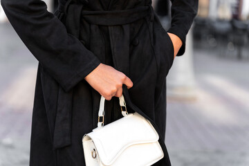 Stylish businesswoman holding white handbag in city