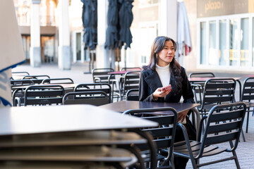 Latina businesswoman holding phone sitting at urban cafe