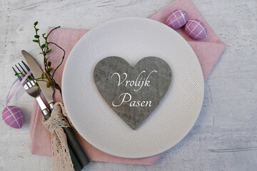 Tafeldecoratie met borden, bestek en paasversieringen; een bordje draagt ​​het opschrift "Fijne Pasen".
