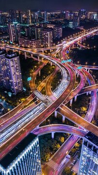 Aerial view of interwoven urban highway during night time with car light trails and city traffic movement vertical video format
