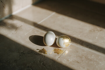 Two decorated eggs resting on a stone surface with sunlight and shadow creating contrast around them
