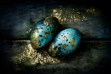 Two decorated eggs with speckled surface and gold accents placed on dark wood