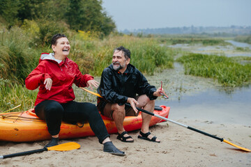 Happy senior couple relaxing by kayak in rain