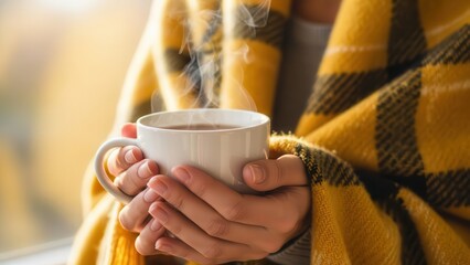 Person holding steaming hot cup of tea wrapped in warm yellow blanket