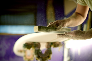 Surfboard, hands and sanding foam in workshop for manufacturing, design or polish. Surf, person and tools to shape blank with block, smooth and production process with dust for creative handcraft