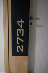 Stylish hotel room sign on wall next to entrance door. Room number 2734, sign in hotel, hostel, or residential complex. Elegant wooden door sign.