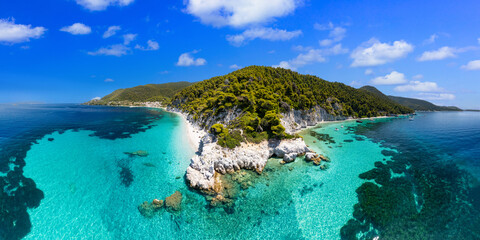 Stunning high-angle aerial panoramic shot of Hovolo Beach on Skopelos island. white limestone cliffs, lush green pine forests reaching the shore, and crystal-clear turquoise waters of the Aegean Sea. 
