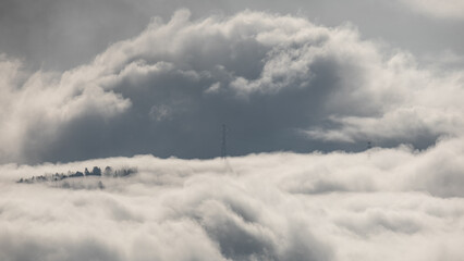 Winter mountain dawn, where a high-voltage pylon rises through rolling clouds and fog, silhouetted against soft morning light.