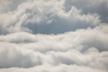 Winter mountain dawn, where a high-voltage pylon rises through rolling clouds and fog, silhouetted against soft morning light.