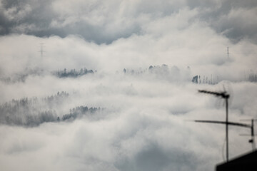 Winter mountain dawn, where a high-voltage pylon rises through rolling clouds and fog, silhouetted against soft morning light.