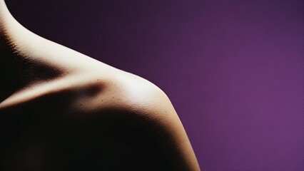 Close-up of healthy human skin on a shoulder and neck, beautifully lit against a minimalist purple background, emphasizing texture and form.
