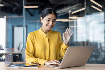 Young Indian businesswoman sitting in the office at her desk, greeting and talking on the laptop camera
